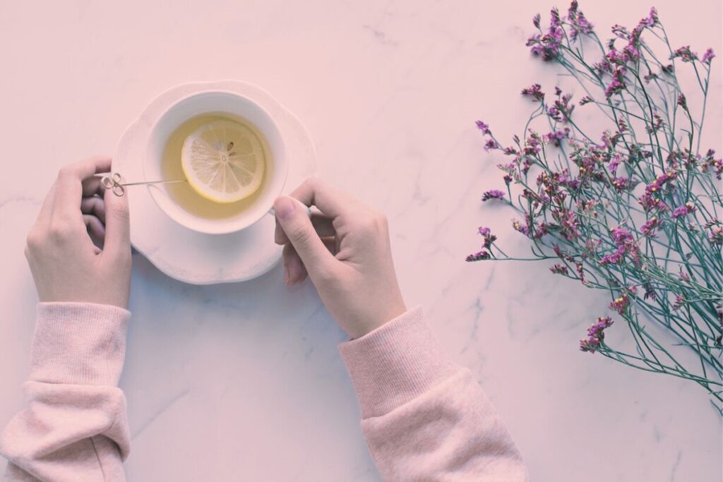 レモンティーを両手でそっと持つ女性の手元と、横に置かれた小さな花が並ぶ、やわらかな雰囲気の写真。