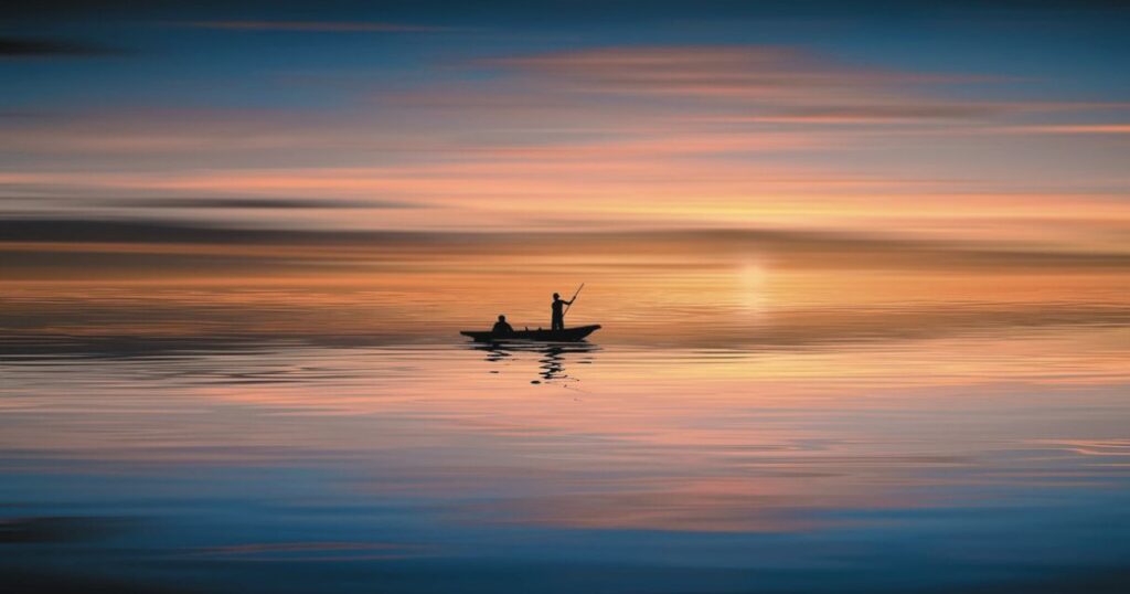夕暮れの湖で静かにボートを進める人のシルエットが映る穏やかな風景