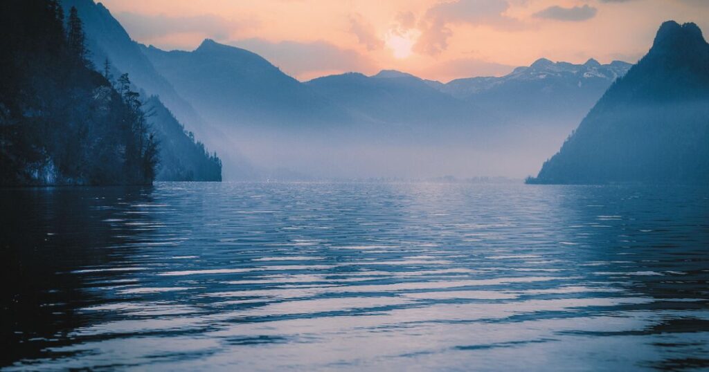 静かな湖と朝の光が差し込む穏やかな風景