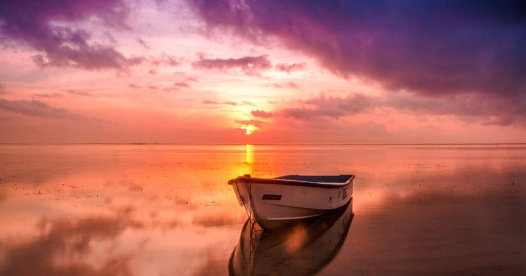 s静かな海で朝日を受けて浮かぶ一艘のボートが映る穏やかな夜明けの風景