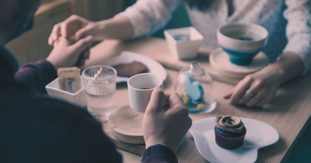 カフェで手をそっと握り合う男女の手元。デート後の静かな距離感を感じる情景。