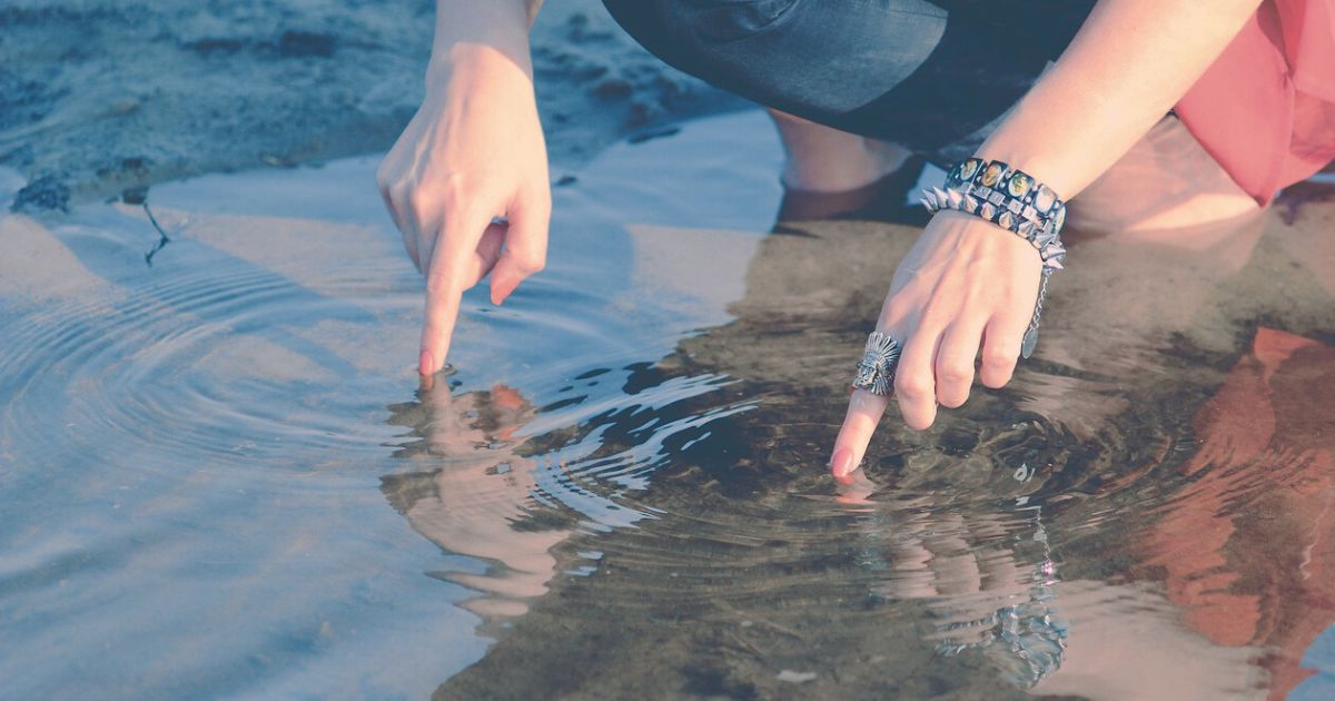 水面にそっと触れて波紋を広げる指先の写真
