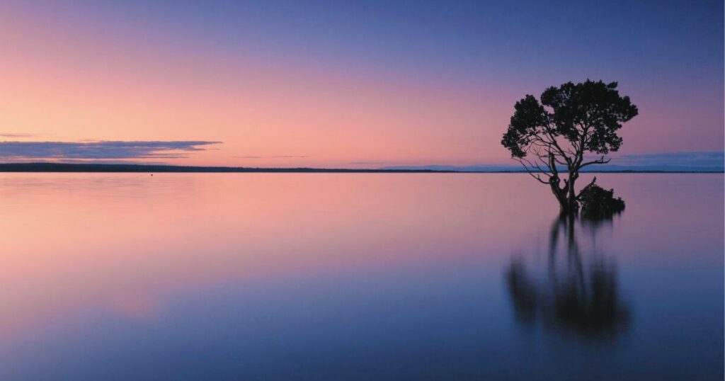 静かな湖面に夕暮れの光が広がる風景。ゆるやかな空の色が心を落ち着かせ、未来へそっと進むような穏やかさを映したイメージ。