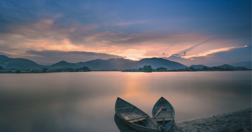 朝日に照らされた静かな湖に二艘のボートが並ぶ風景。穏やかな時間が広がり、未来の安心感を感じられる情景。