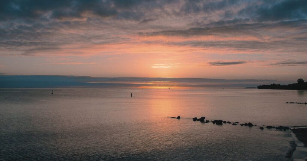 静かな海辺にやわらかな朝日が差し込む、希望を感じる日の出の風景