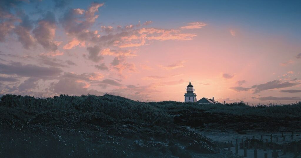 夕暮れの空に灯台が静かに立つ、穏やかな海辺の風景