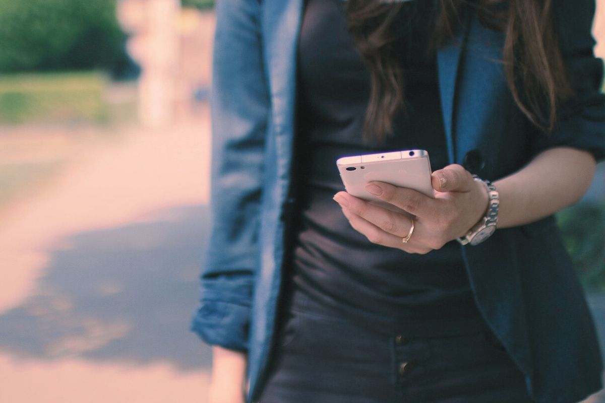 屋外でスマホの画面をそっと見つめる女性の手元。LINEの返信を待ちながら、少し気持ちが揺れている場面を思わせる写真。