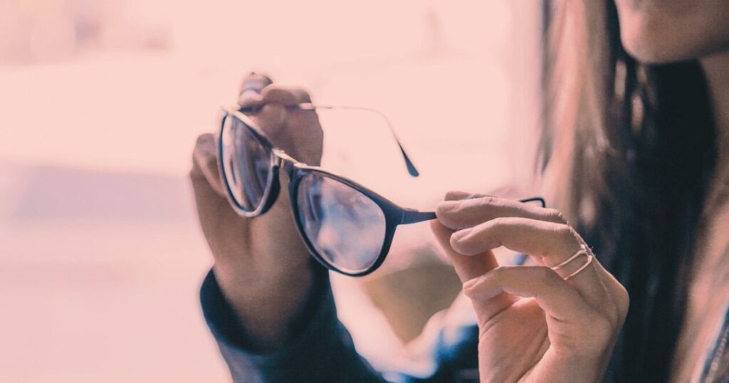 柔らかな光の中でメガネをそっと持ち上げて見つめる女性の手元の写真
