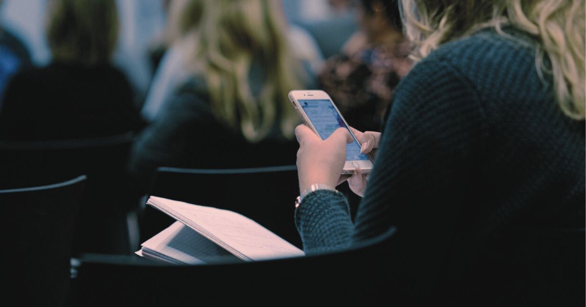 教室でスマホのメッセージを見つめる女性の後ろ姿