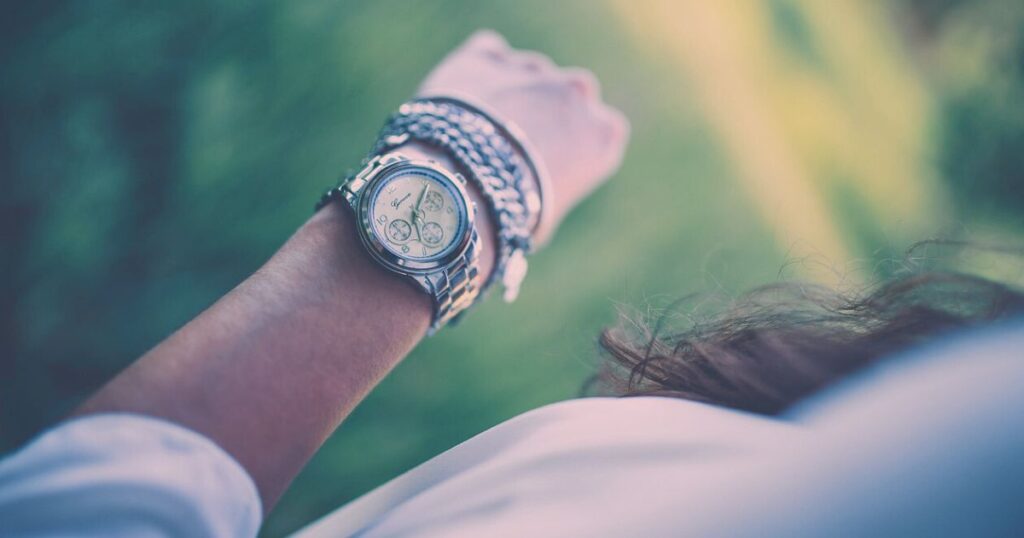 柔らかな光の中で腕時計をつけた女性の手元が映る静かな写真